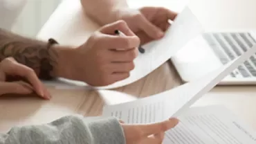 People reviewing documents at a desk with a laptop.