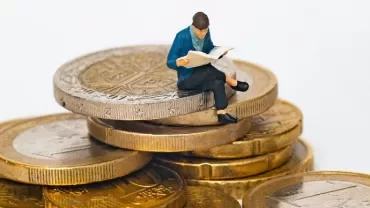 Figure reading a newspaper while sitting on a stack of coins.